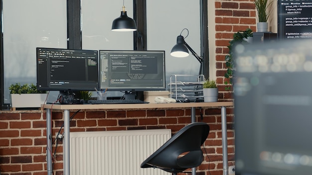 Desk with multiple computer monitors displaying parsing code and programming language compiling in empty software developing agency office. Servers cloud computing big data algorithms.