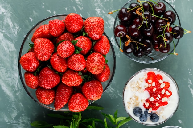 Dessert in a vase with strawberries, blueberries, mint, cherries flat lay on a plaster surface