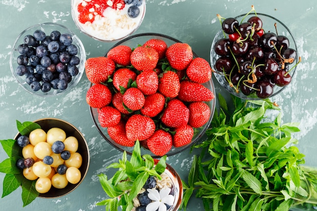 Free Photo dessert with strawberries, blueberries, mint, cherries in vase and goblet on plaster surface, flat lay.