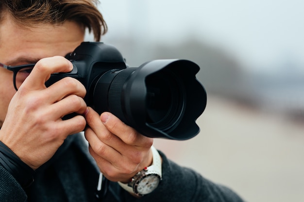 Detail view of young man in eyeglasses taking photos on the street.