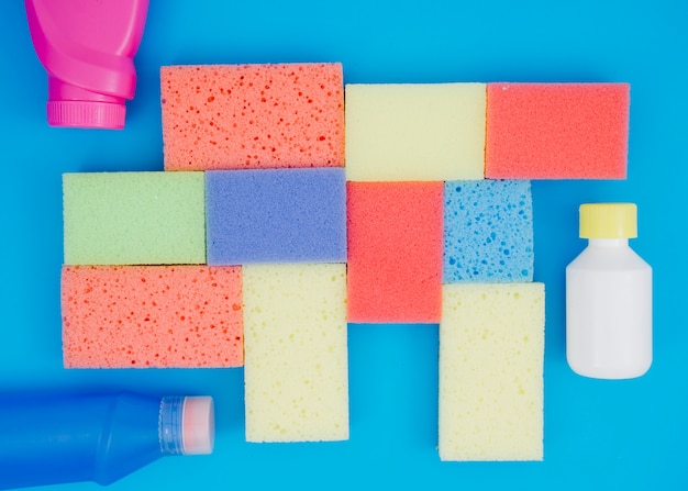 Free Photo detergent bottle near the multi colored sponges on blue background