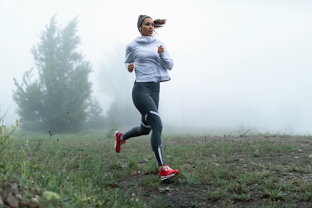 Determined female runner jogging through misty filed in the morning Copy space