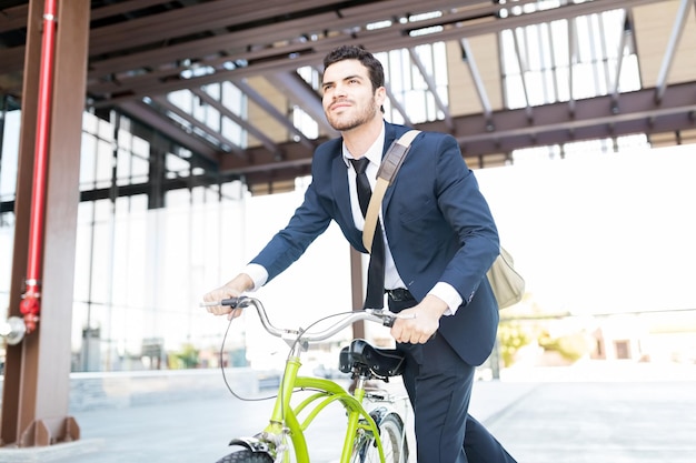 Free photo determined manager in elegant suit riding vintage bicycle in city