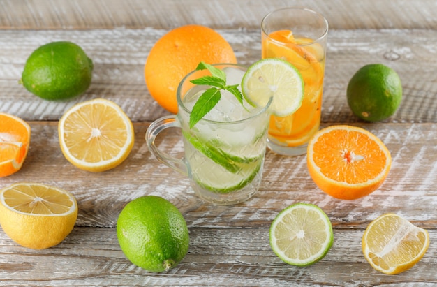 Free photo detox water with limes, lemons, oranges, mint in cup and glass on wooden surface, high angle view.