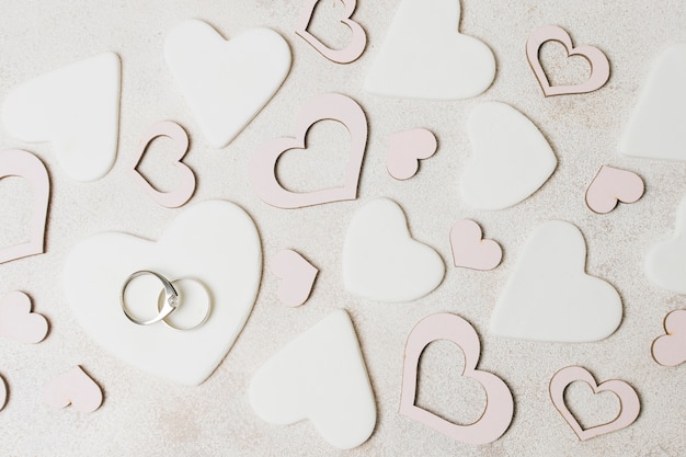 Diamond wedding rings on white and pink heart shape over the concrete backdrop