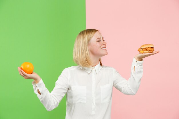 Diet. Dieting concept. Healthy Food. Beautiful Young Woman choosing between fruits and unhelathy fast food