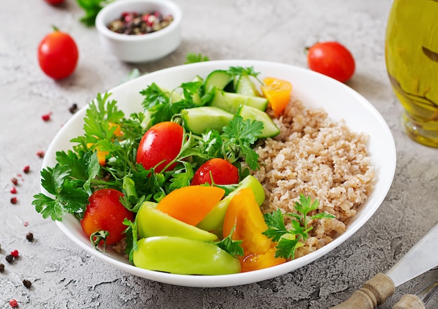 Diet menu. Healthy vegetarian salad of fresh vegetables - tomatoes, cucumber, sweet peppers and porridge on bowl. Vegan food.