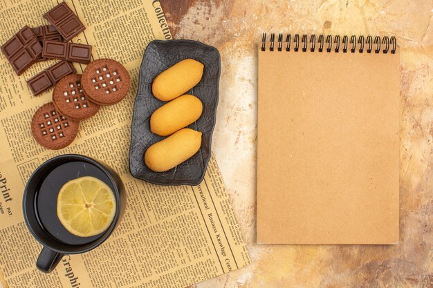 Different biscuits and tea in a black cup and notebook on mixed color table