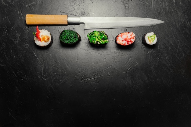 Different Sushi with Japanese knife on black stone slate background. Sushi on a table.