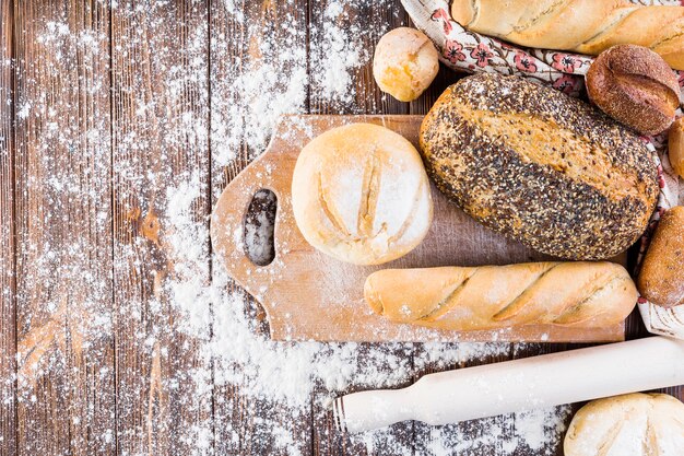 Different type of baked breads with flour on the wooden table