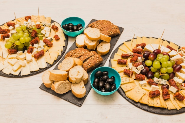 Free photo different type of bread slices with olives and platter cheese on wooden desk