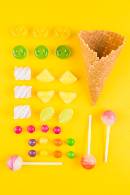 Different type of candies and ice-cream waffle cone on yellow backdrop