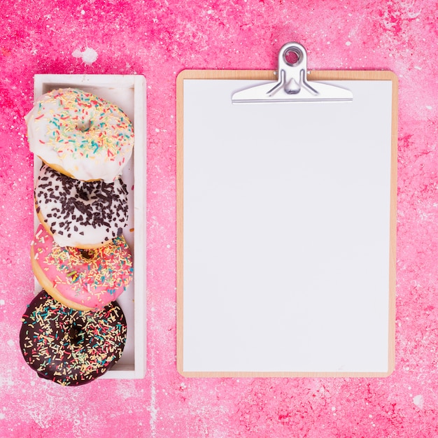 Free Photo different type of donuts in white rectangular box near the clipboard with white paper against pink background