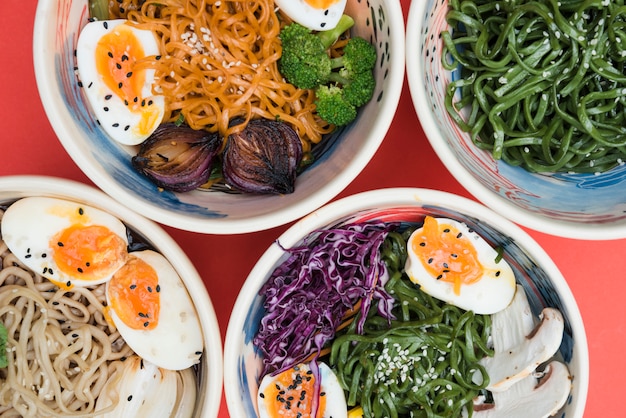 Different type of noodles with eggs; seaweeds and salad in the bowl on red backdrop