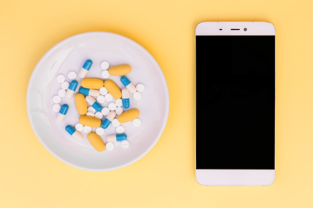 Free Photo different type of pills on white plate near the smartphone on yellow background