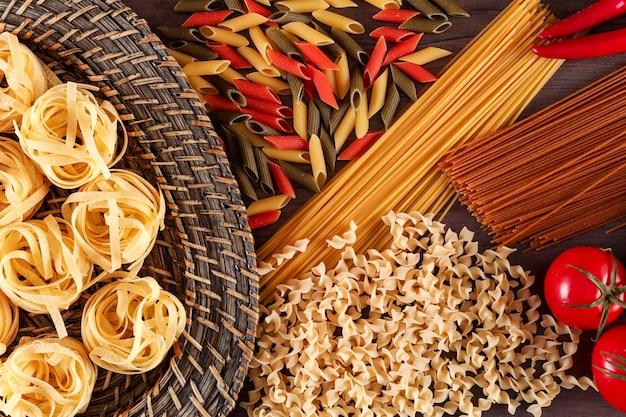 different types of pasta with red chili peppers and tomatoes on a wooden surface top view