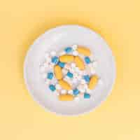 Free photo different types of pills on white plate over yellow background