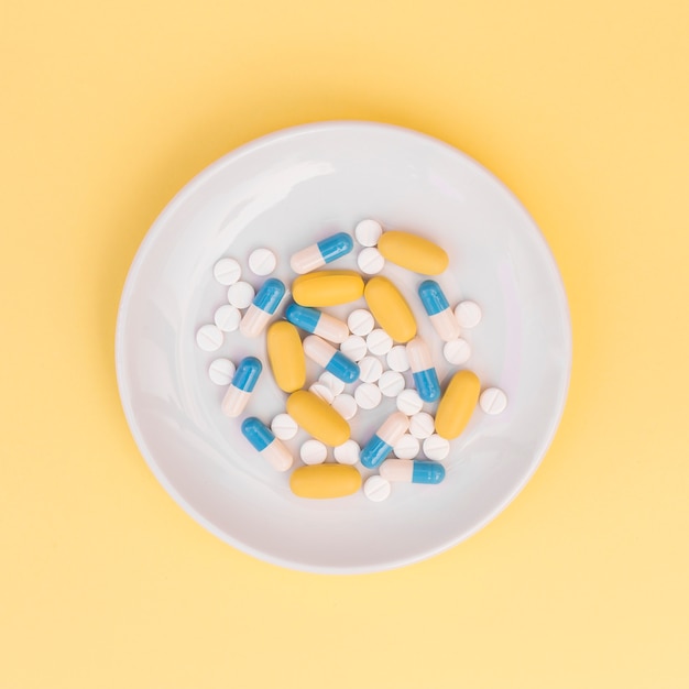 Free Photo different types of pills on white plate over yellow background