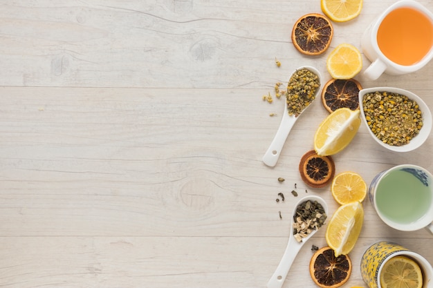 Free photo different types of tea in ceramic cup with herbs and dry grapefruit slices on desk