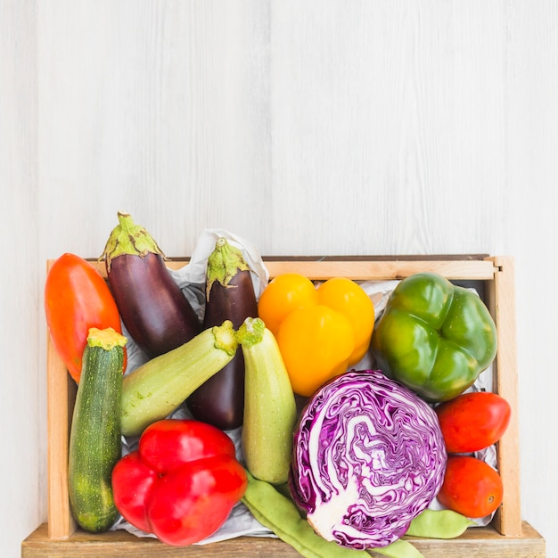 Different types of vegetables in container on wooden backdrop