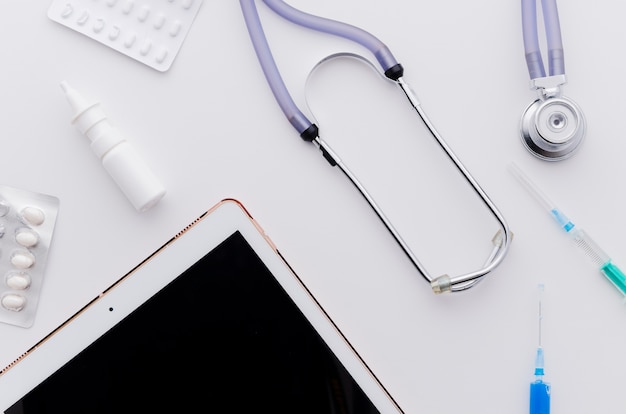 Free photo digital tablet; pills; stethoscope and syringe on white backdrop