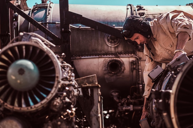 Free photo diligent worker is focused on jet's engine. he is wearing a helmet and a uniform.