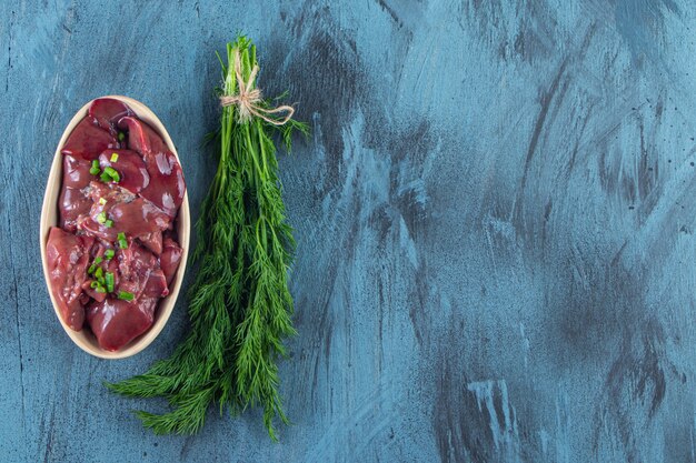 Dill bunch and bowl of chicken livers , on the blue background. 