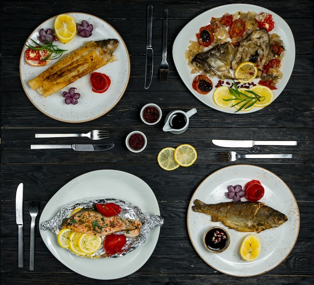 Dinner menu set for 4 pax, different fish , seafood meals in white plates with cutlery and sauces