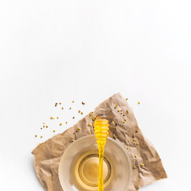 Free Photo dipper on bowl of honey with bee pollen seeds over brown paper