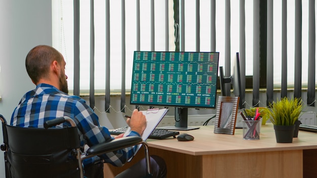 Free Photo disabled businessman sitting in wheelchair immobilized checking financial economy data taking notes in business office discussing with colleague. handicapped freelancer using modern technology.