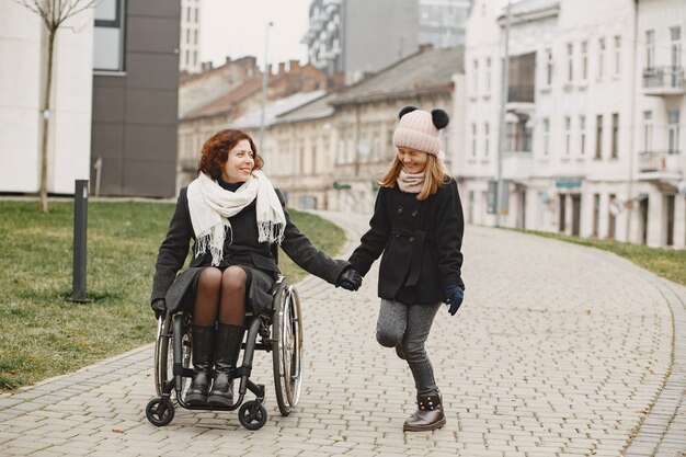 Disabled woman in wheelchair with daughter. Family walking outside at park.