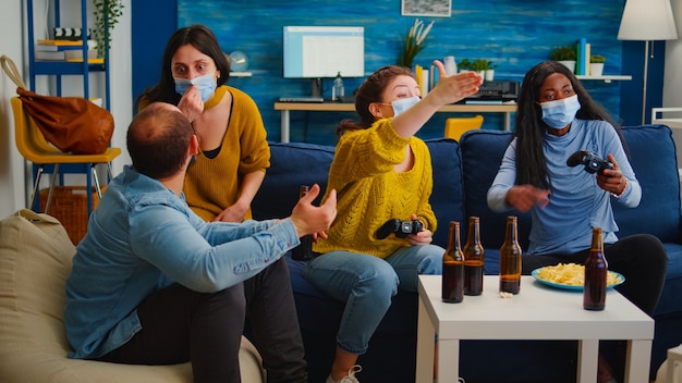 Free photo disappointed diverse people loosing playing video games at home respecting social distancing because of corona outbreak wearing face mask against spreading virus. new normal party social distance