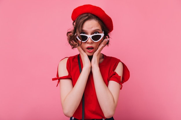 Disappointed french female model posing in sunglasses. unhappy short-haired woman in red beret isolated.