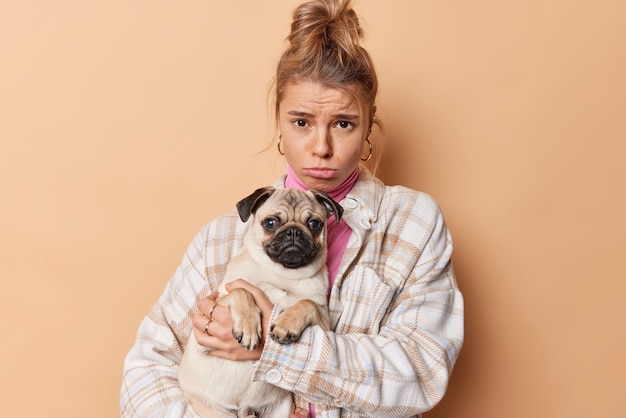 Free Photo disappointed frustrated young female pet owner sad because of illness of dog go together to vet clinic dressed in casual clothes isolated over beige background. people animals and care concept