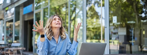 Disappointed young businesswoman feeling frustrated sitting with laptop outdoors on street looking