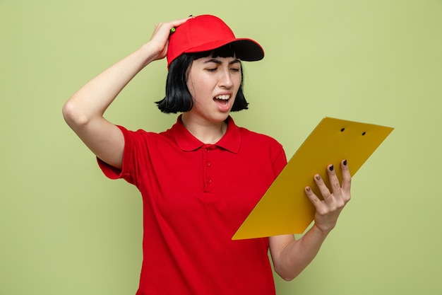 Disappointed young caucasian delivery woman holding and looking at clipboard 