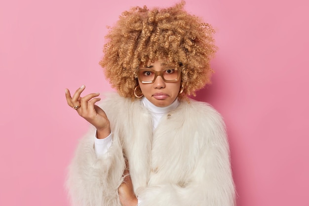 Free Photo discontent unhappy curly haired woman shrugs shoulder feels indignant faces difficult choice has sad expression wears eyeglasses white coat isolated over pink background. so what should i do