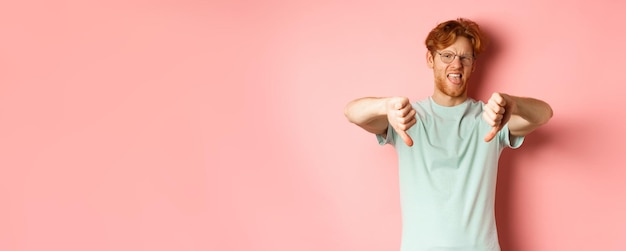 Free photo disgusted redhead man in tshirt and glasses showing thumbs down and tongue grimacing from aversion s