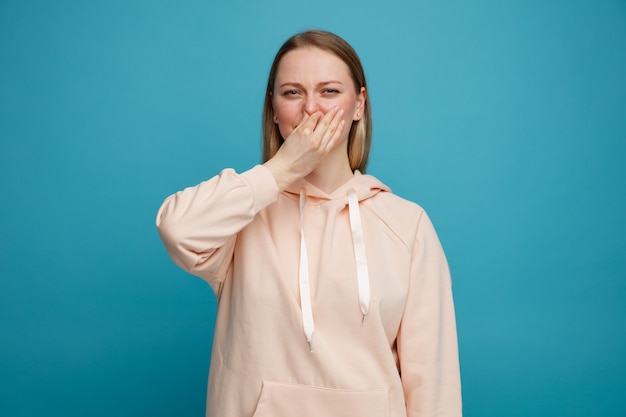 Disgusted young blonde woman doing bad smell gesture 