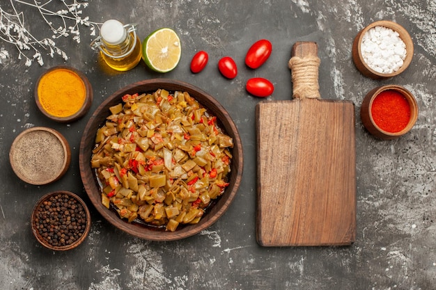 Free Photo dish of green beans plate of green beans lemon bottle of oil colorful spices and tomatoes in the bowls next to the cutting board