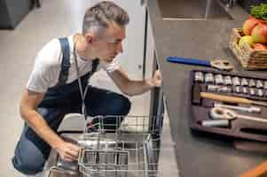 Free photo dishwasher repair top view of middleaged man crouching near open dishwasher