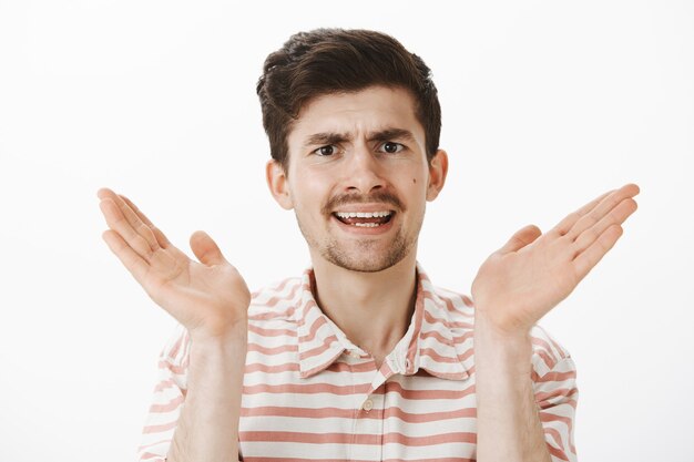 displeased annoyed ordinary caucasian male with moustache, raising palm near face and arguing, being displeased and frustrated, hearing nonsense over gray wall