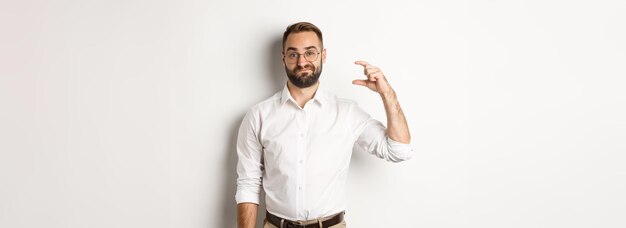 Displeased bearded businessman showing small gesture looking disappointed standing against white bac