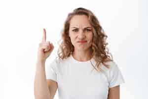 Free photo displeased blond woman grimacing looking disappointed and skeptical pointing finger up at something bad and upsetting complaining white background