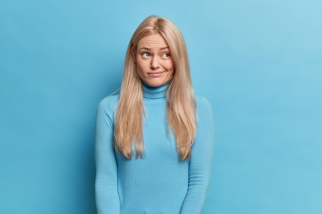 Free photo displeased blonde young woman with long hair looks upset aside has thoughtful expression purses lips wears turtleneck