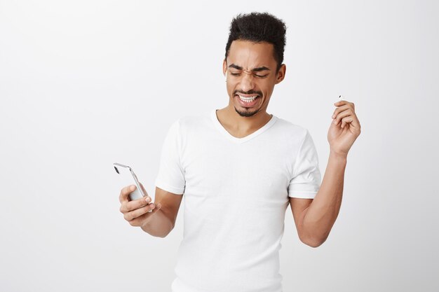 Displeased and bothered african-american guy take-off earphone from loud awful noise, stop music on mobile phone