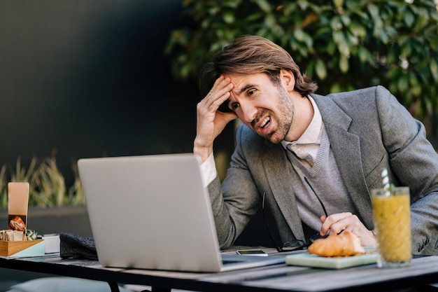 Displeased businessman working on laptop while sitting in outdoors cafe.