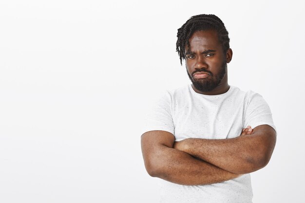 displeased guy with braids posing against the white wall