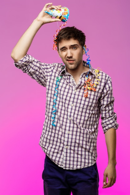 Free Photo displeased tired man at birthday party over purple wall.