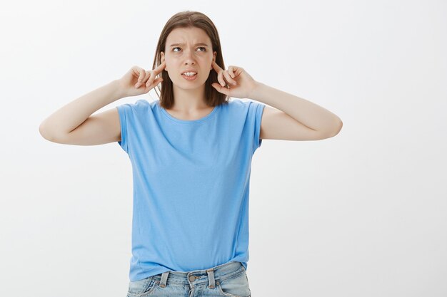 Displeased young female student complaining loud neighbours, shut ears with fingers